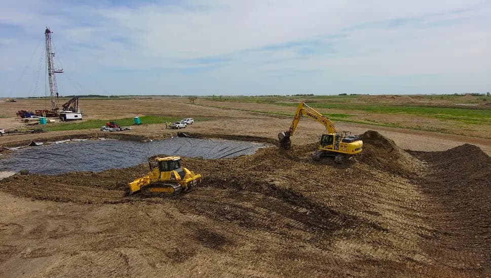 Dozer and excavator moving material at Amanda Kunkel 2, a drilling rig on the horizon.